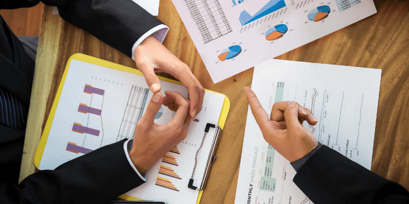 Various financial charts are spread out on a table as a financial advisor and clients engage in a discussion about financial planning strategies.