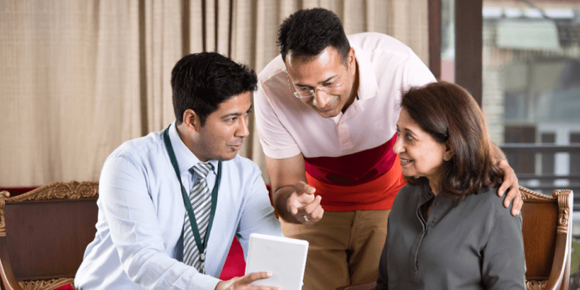 An investment advisor giving investment advice to a couple in a cozy home setting, using a tablet to present financial information and charts, reflecting a personal and engaging financial consultation.